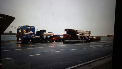 drayage of 18-wheeler flat rack delivers crane to port where cargo ship waits for loading